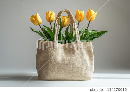 Reusable shopping bag made of fabric with a bouquet of yellow tulips on a white background. Reusable shopping bag made of fabric with a bouquet of yellow tulips on a white background. 134270016