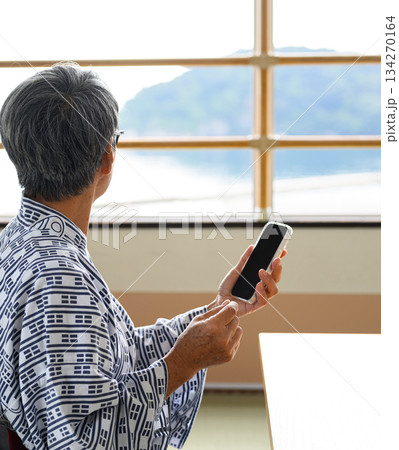 浴衣のシニアが窓から海を眺めスマホ操作 134270164