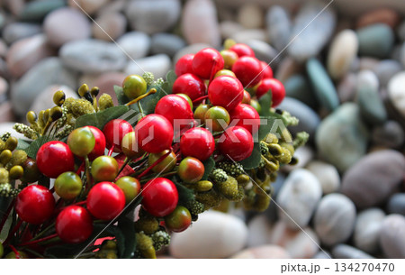 Decorative Wreath With Artificial Berries And Branches On Defocused Smooth Rocks Backdrop  134270470