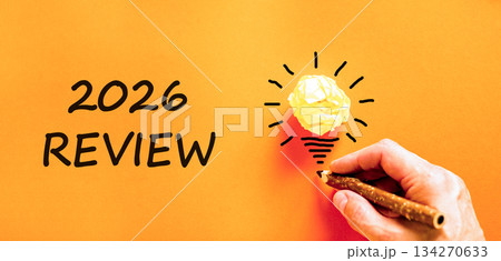 2026 Review symbol. Concept words 2026 Review on beautiful orange paper. Beautiful orange paper background. Light bulb icon. Businessman's hand with pen. Business and 2026 review concept. Copy space. 2026 Review symbol. Concept words 2026 Review on beautiful orange paper. Beautiful orange paper background. Light bulb icon. Businessman's hand with pen. Business and 2026 review concept. Copy space. 134270633
