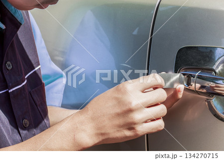 Close-up Of Person's Young Man Locksmith Hand Opening white Car Door With Lock picker. 134270715