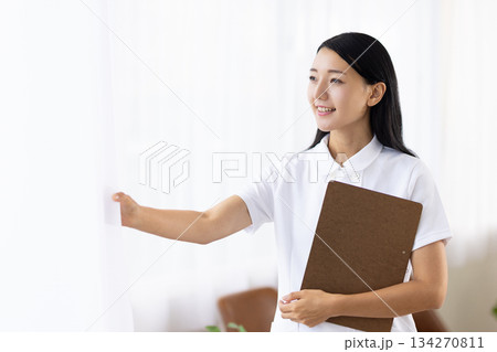 笑顔でカーテンを開ける白衣姿の女性 134270811