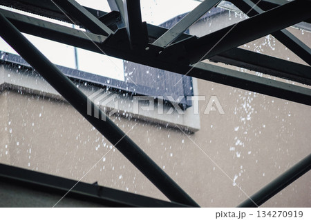 Heavy rain pouring off a black tiled roof and metal gutter below a modern, transparent canopy structure 134270919