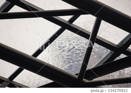 Rain falling on a transparent glass roof with water dripping from the dark metal support structure below Rain falling on a transparent glass roof with water dripping from the dark metal support structure below 134270922