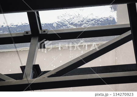 Rain falling on a transparent glass roof with water dripping from the dark metal support structure below Rain falling on a transparent glass roof with water dripping from the dark metal support structure below 134270923