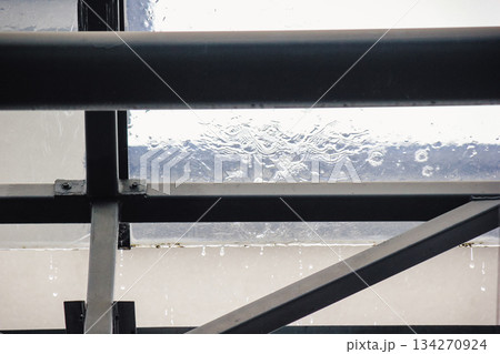 Rain falling on a transparent glass roof with water dripping from the dark metal support structure below Rain falling on a transparent glass roof with water dripping from the dark metal support structure below 134270924