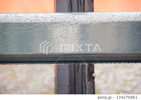 Close up of a smooth, grey metal railing covered in fresh rain drops with a blurred orange background 134270961