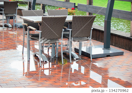 Empty wicker chairs and tables on a wet cafe patio reflecting in the brick pavement after rain 134270962