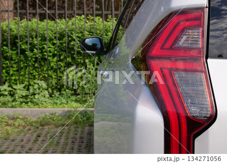 Rear LED Lights Of Large SUV With Fence And Green Hedge On Background Rear LED Lights Of Large SUV With Fence And Green Hedge On Background 134271056