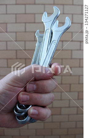 Clenched Human Fist With Different Open End Wrenches Over Brick Wall 134271127
