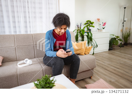 Young woman using smartphone sitting on sofa in living room Young woman using smartphone sitting on sofa in living room 134271132