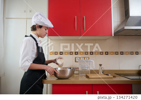 Young Chef In White Uniform Preparing Batter In A Red Modern Studio Kitchen At Home Young Chef In White Uniform Preparing Batter In A Red Modern Studio Kitchen At Home 134271420