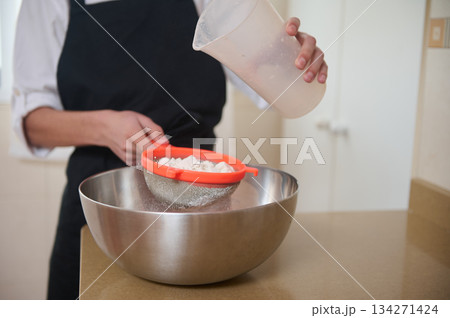 Chef Pours Flour Through A Sieve Into A Large Mixing Bowl In Kitchen 134271424