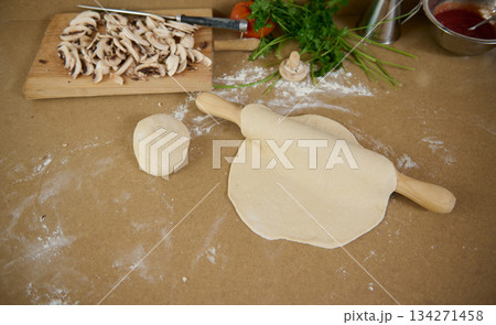 Fresh Dumpling Dough Rolling On Kitchen Table with Mushrooms, Herbs, and Flour 134271458