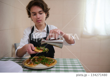 Young Chef In Apron Pouring Sauce On Fresh Pizza In A Cozy Home Kitchen 134271480