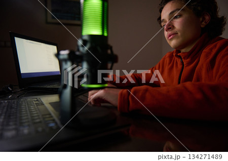 Young Boy Recording Podcast At Home With Laptop And Green Microphone Studio Setup Night Lights Young Boy Recording Podcast At Home With Laptop And Green Microphone Studio Setup Night Lights 134271489