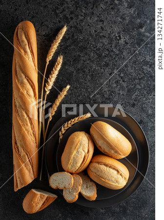 Baguette, French buns, and wheat ears on a black stone table. Baguette, French buns, and wheat ears on a black stone table. 134271744