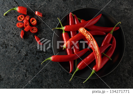 Fresh red chili peppers with green stems on a black stone table. 134271771