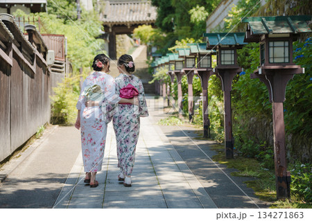 神社の参道で木灯籠のそばを歩く浴衣姿の若い女性2人。京都市、京都府、日本 神社の参道で木灯籠のそばを歩く浴衣姿の若い女性2人。京都市、京都府、日本 134271863