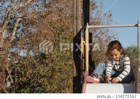 Childhood moments: a contented girl with her toys on a playground slide in the sun Childhood moments: a contented girl with her toys on a playground slide in the sun 134272162