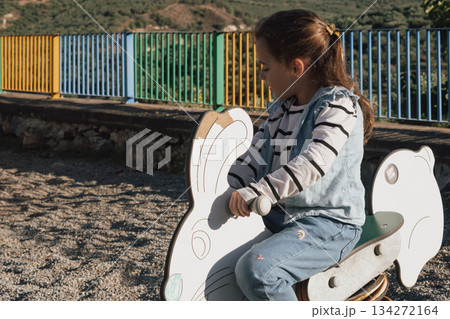 Playground fun: a child on a colourful spring toy in the shape of a bunny or rabbit 134272164