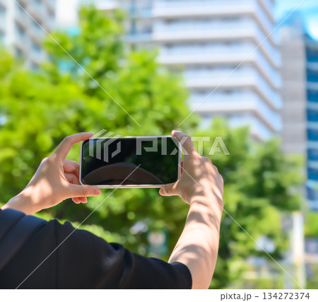 夏の都市でスマートフォンを横向きに持ち、景色を動画撮影する女性の上半身 夏の都市でスマートフォンを横向きに持ち、景色を動画撮影する女性の上半身 134272374
