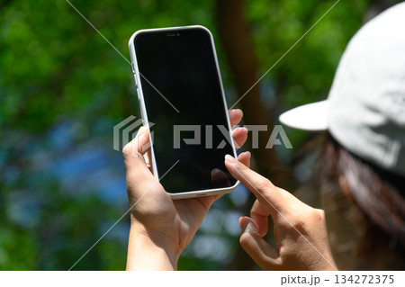 屋外でスマートフォンを操作する若い女性の手元と帽子 134272375
