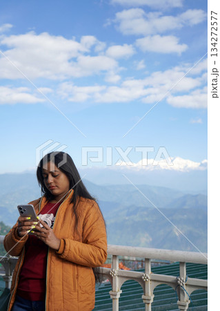 Young woman using smartphone while standing against a scenic Himalayan mountain backdrop 134272577