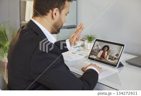 Man having video call meeting and waving hand at tablet screen, greeting his business colleague 134272911