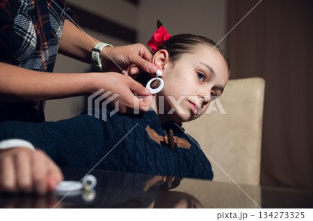 Young Girl Getting Ears Pierced With White Hoop Earrings, Helped By Caregiver 134273325