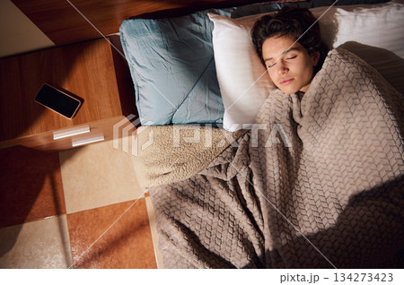 Person Sleeping In Bed With Cozy Blanket, Pillow, And Phone On Nightstand 134273423