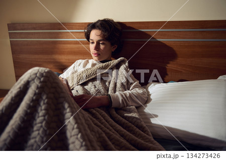 Young Woman Relaxing in Bed Wrapped in Cozy Blanket, Reading at Night Young Woman Relaxing in Bed Wrapped in Cozy Blanket, Reading at Night 134273426