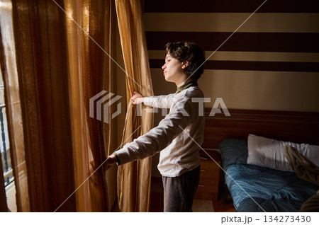 Contemplative Woman Opens Curtains To Let Morning Light In Cozy Bedroom 134273430