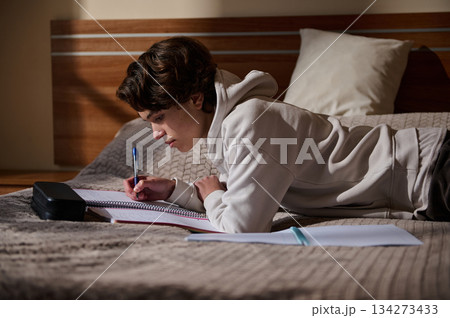 Student Lying on Bed Studying With Notebook and Pen in Cozy Bedroom 134273433