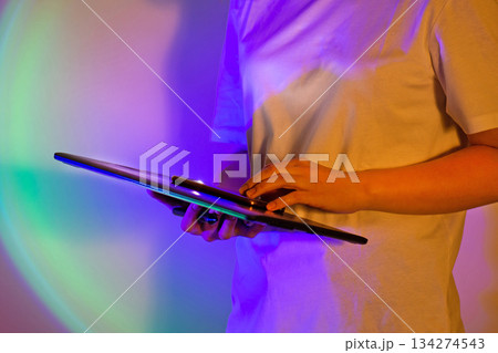 Vibrant work setting and young woman in white shirt with digital tablet in neon bright saturated lights. Power of tech and neon artistry. 134274543