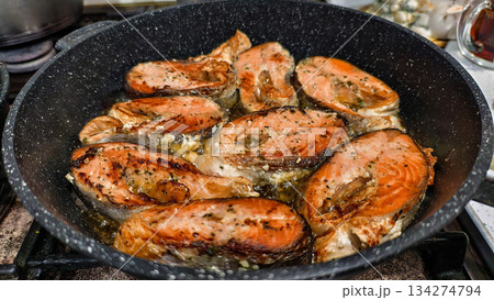Fried salmon pieces, seasoned with herbs and pepper, sizzle in a frying pan. The golden crust glistens with oil as the pan sits on the stove. A home cook is searing fish fillets for dinner. Fried salmon pieces, seasoned with herbs and pepper, sizzle in a frying pan. The golden crust glistens with oil as the pan sits on the stove. A home cook is searing fish fillets for dinner. 134274794