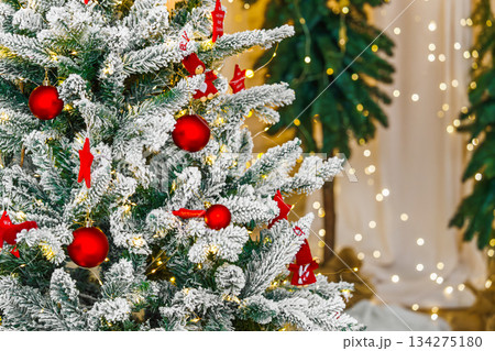 Snowy Christmas tree branches adorned with red ornaments and sparkling lights, holiday background Snowy Christmas tree branches adorned with red ornaments and sparkling lights, holiday background 134275180