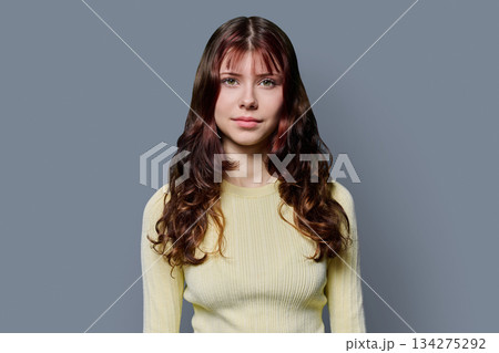 Portrait of smiling teenage girl with curly long hair on gray background Portrait of smiling teenage girl with curly long hair on gray background 134275292