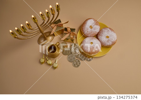 Hanukkah Celebration Setup. A menorah, dreidels, gift boxes, and donuts on a beige background 134275374