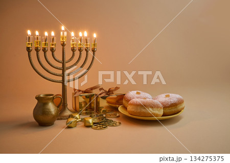 Hanukkah Celebration Setup. A menorah, dreidels, gift boxes, and donuts on a beige background 134275375