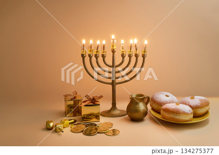 Hanukkah Celebration Setup. A menorah, dreidels, gift boxes, and donuts on a beige background 134275377