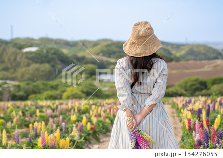 花畑を歩く麦わら帽子とワンピースの若い女性の後ろ姿 花畑を歩く麦わら帽子とワンピースの若い女性の後ろ姿 134276055