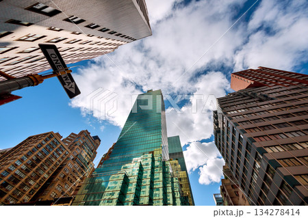 Manhattan skyscrapers loom above in busy New York City street with clouds in blue sky Manhattan skyscrapers loom above in busy New York City street with clouds in blue sky 134278414