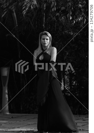 A beautiful Caucasian blonde is walking in nature wearing a black dress. The luxury of the territory of an expensive hotel. 134279706