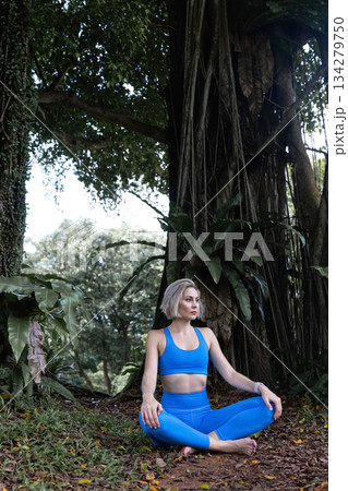 A beautiful girl with light hair is practicing yoga or meditation in the park 134279750