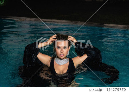 A sexy girl in a black swimsuit poses at night by the pool at a party.  134279770