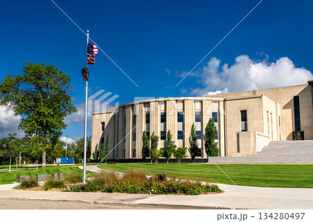 North Dakota State Capitol Legislative Wing stands in Bismarck, USA. Art Deco limestone building features curved facade and American flag under blue sky North Dakota State Capitol Legislative Wing stands in Bismarck, USA. Art Deco limestone building features curved facade and American flag under blue sky 134280497