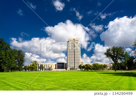 North Dakota State Capitol building stands on green lawn in Bismarck, USA. Art Deco skyscraper features white limestone facade under blue sky North Dakota State Capitol building stands on green lawn in Bismarck, USA. Art Deco skyscraper features white limestone facade under blue sky 134280499