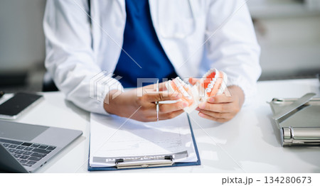 Dentist sitting at table with jaw samples tooth model and working with tablet and laptop. professional dental clinic. Dentist sitting at table with jaw samples tooth model and working with tablet and laptop. professional dental clinic. 134280673