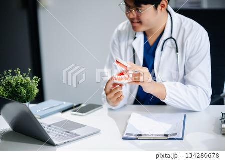 Dentist sitting at table with jaw samples tooth model and working with tablet and laptop. professional dental clinic. 134280678